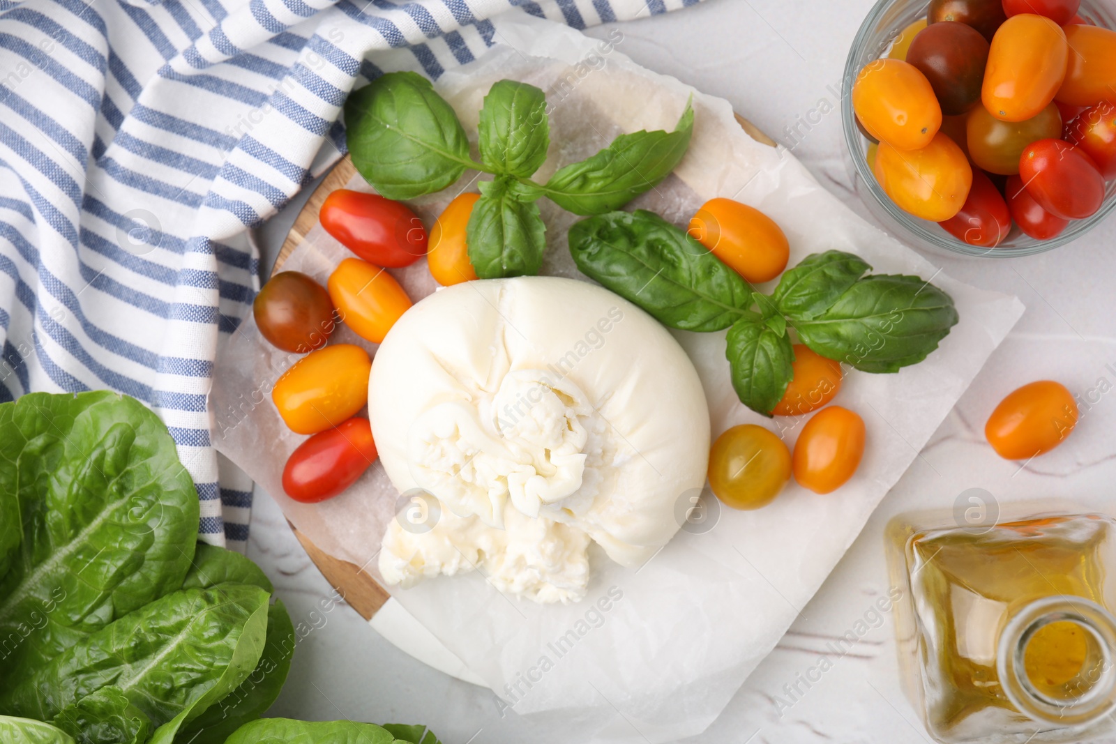 Photo of Delicious fresh burrata cheese with basil leaves, tomatoes and oil on white textured table, flat lay