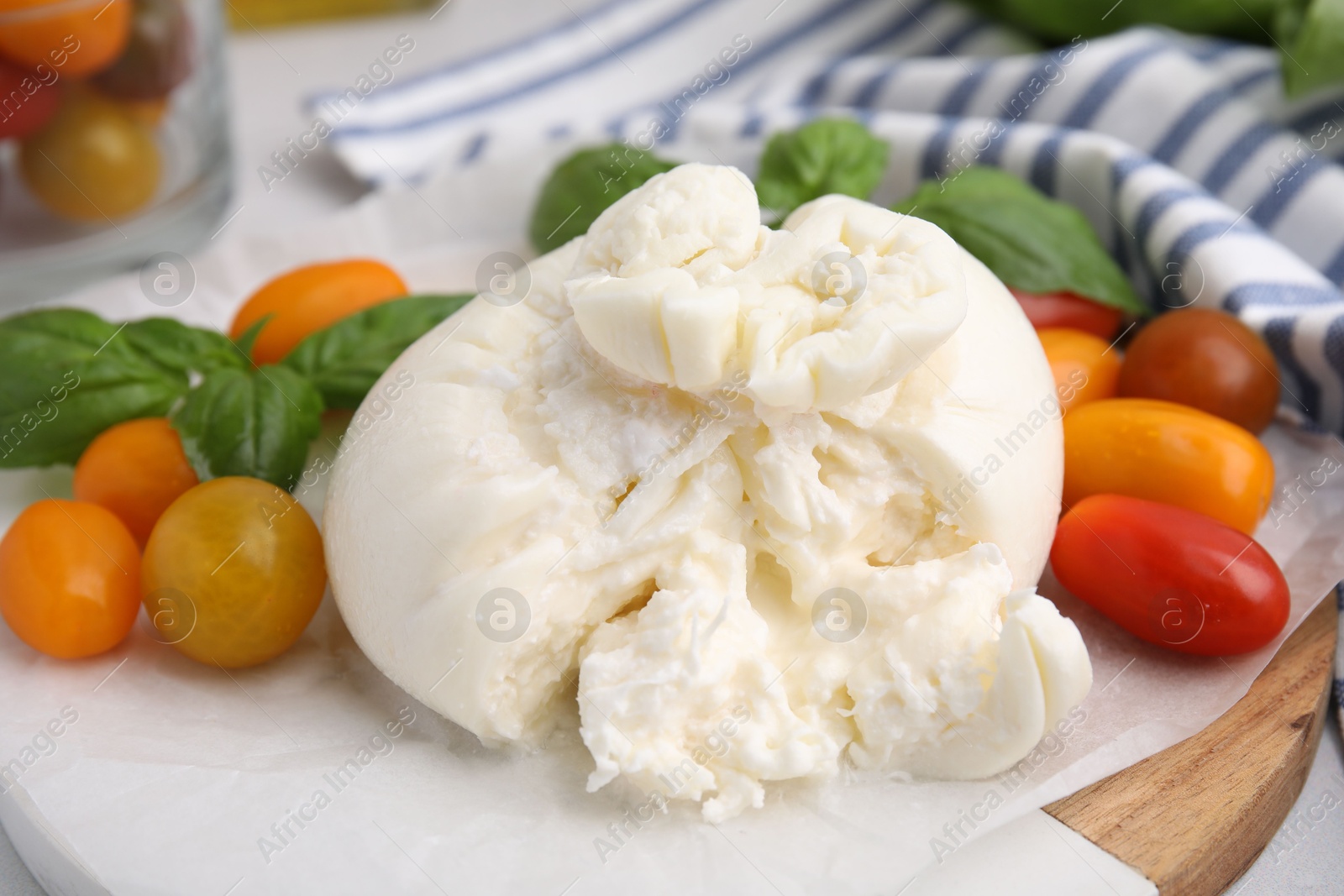 Photo of Delicious fresh burrata cheese with basil leaves and tomatoes on white table, closeup