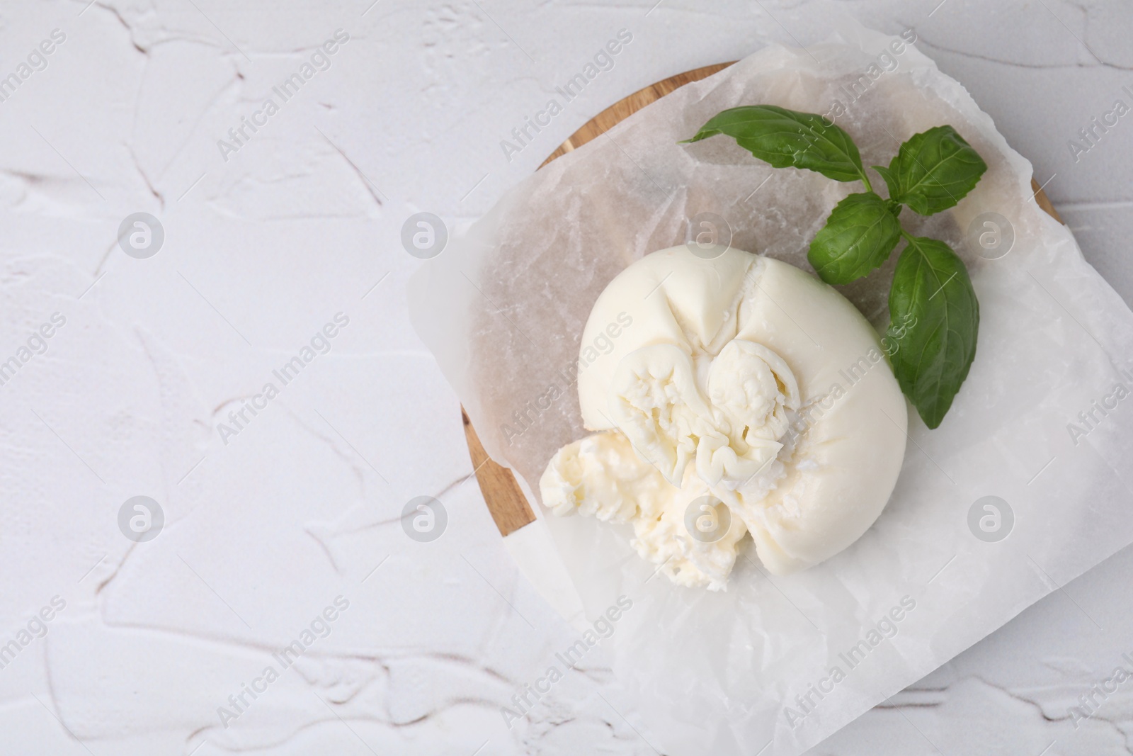 Photo of Delicious fresh burrata cheese with basil leaves on white textured table, top view. Space for text