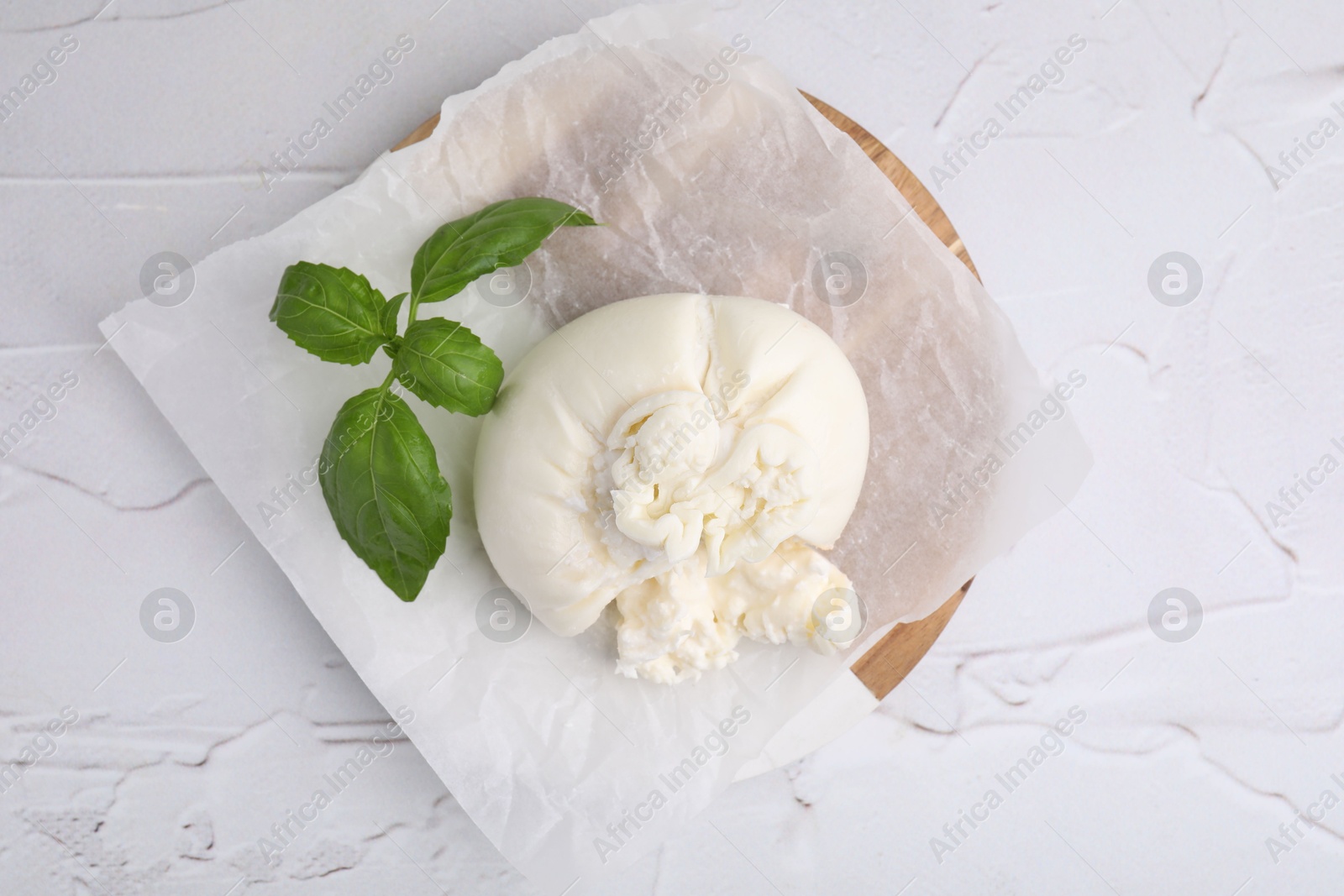 Photo of Delicious fresh burrata cheese with basil leaves on white textured table, top view