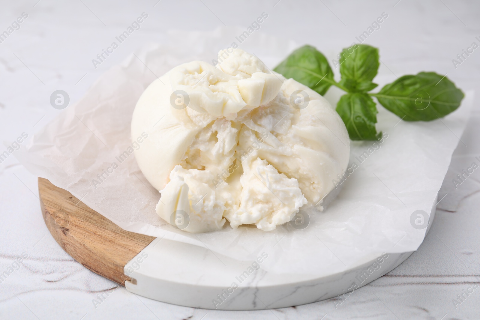 Photo of Delicious fresh burrata cheese with basil leaves on white textured table