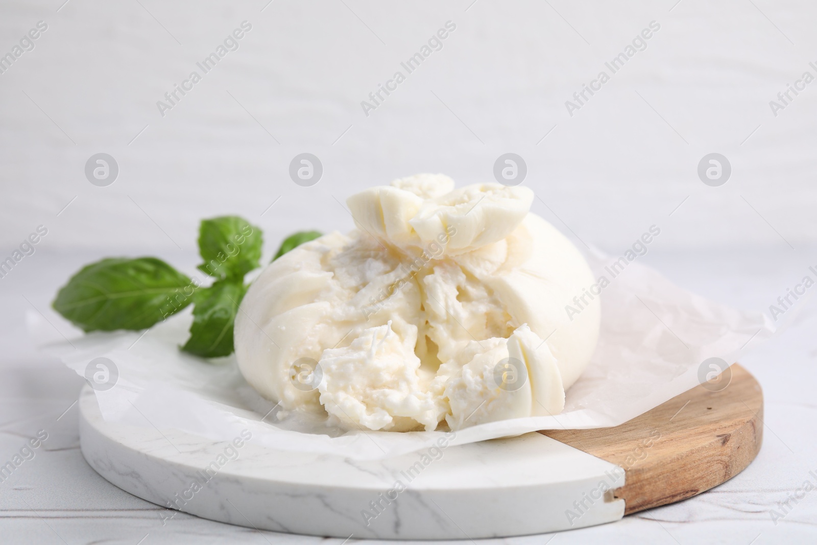 Photo of Delicious fresh burrata cheese with basil leaves on white textured table, closeup