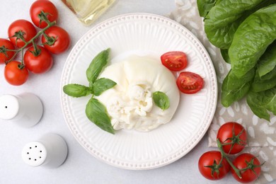 Photo of Delicious burrata cheese, tomatoes, basil and spinach on light table, flat lay