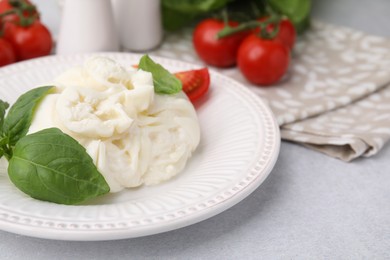 Photo of Delicious burrata cheese, tomatoes and basil on light table, closeup