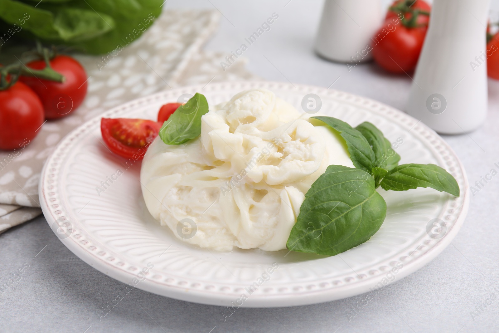 Photo of Delicious burrata cheese, tomatoes and basil on light table, closeup