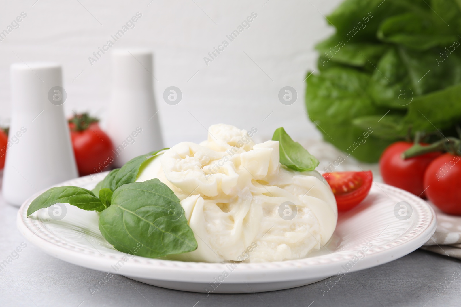 Photo of Delicious burrata cheese, tomatoes and basil on light table, closeup