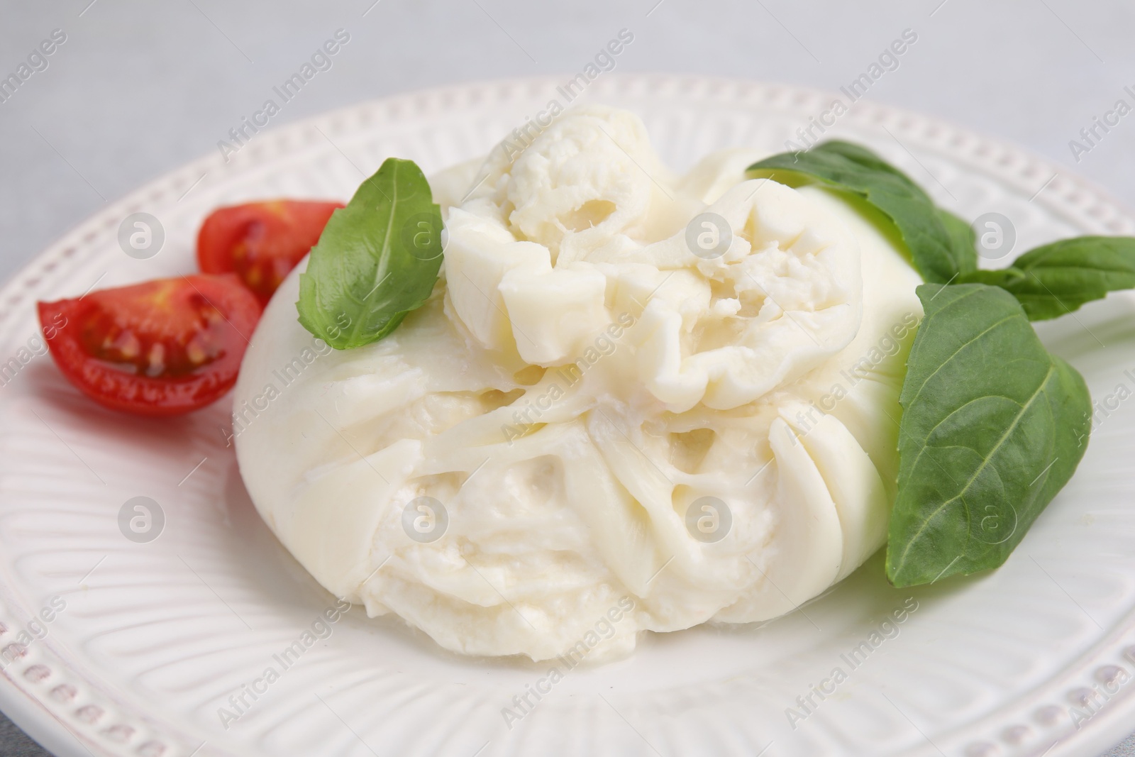 Photo of Delicious burrata cheese, tomatoes and basil on table, closeup