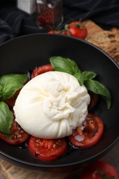 Delicious burrata cheese, tomatoes and basil in bowl, closeup