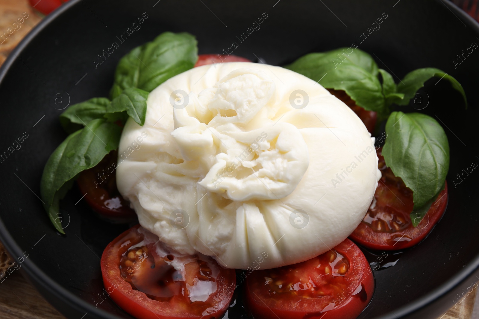 Photo of Delicious burrata cheese, tomatoes and basil in bowl, closeup