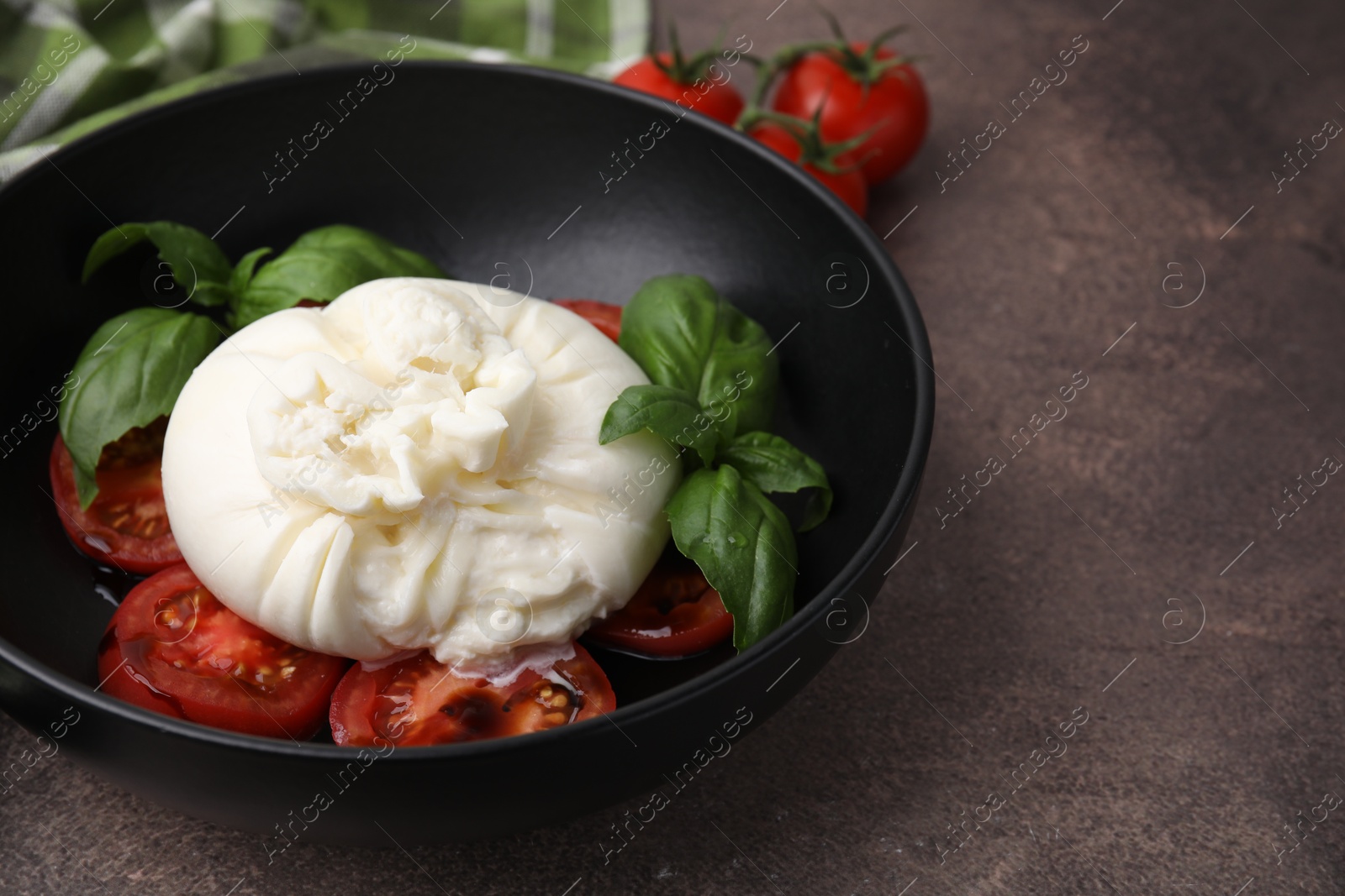 Photo of Delicious burrata cheese, tomatoes and basil in bowl on brown table, closeup. Space for text