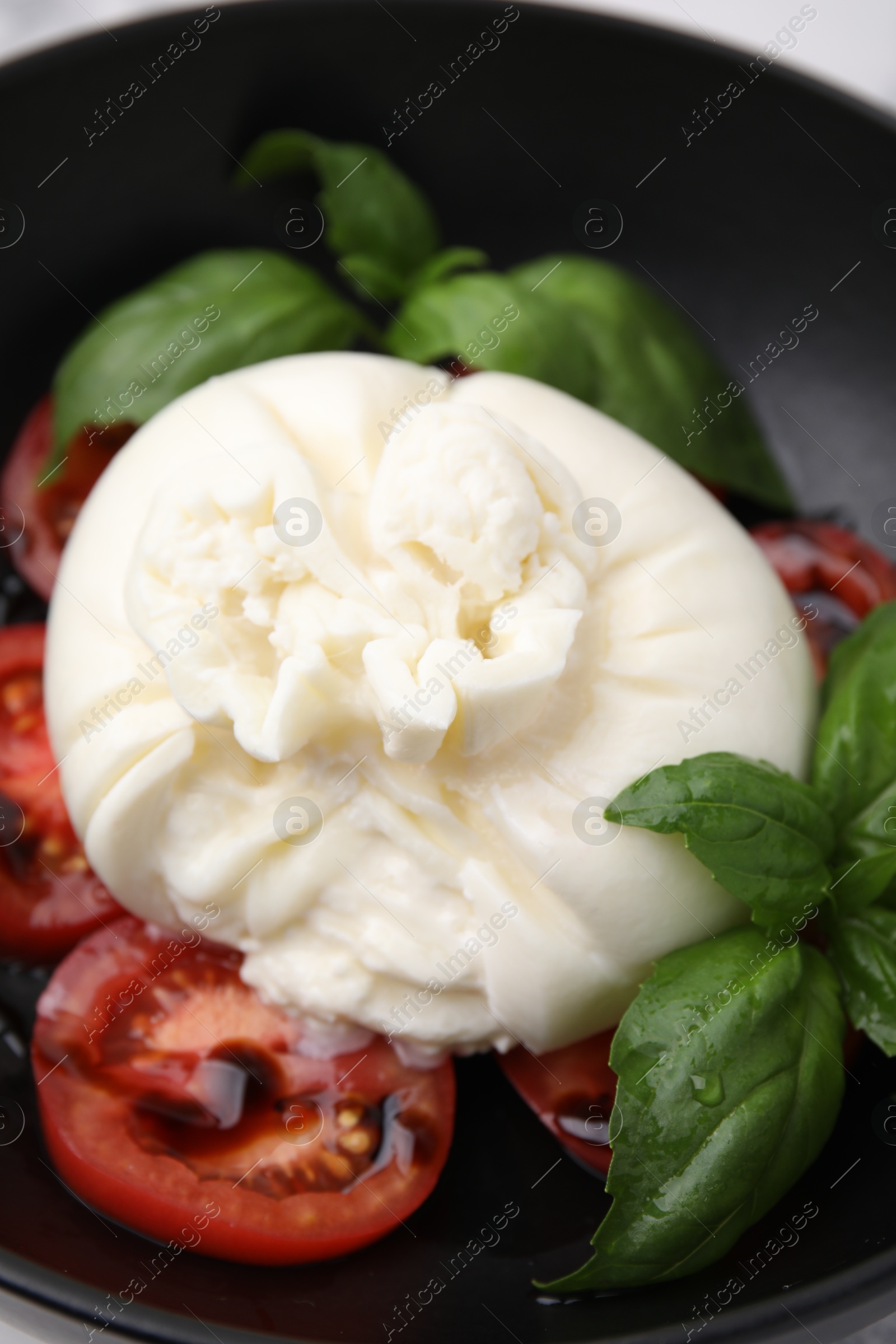 Photo of Delicious burrata cheese, tomatoes and basil in bowl, closeup