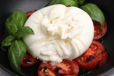 Delicious burrata cheese, tomatoes and basil in bowl, closeup