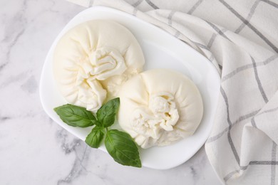 Photo of Delicious burrata cheese and basil on white marble table, top view