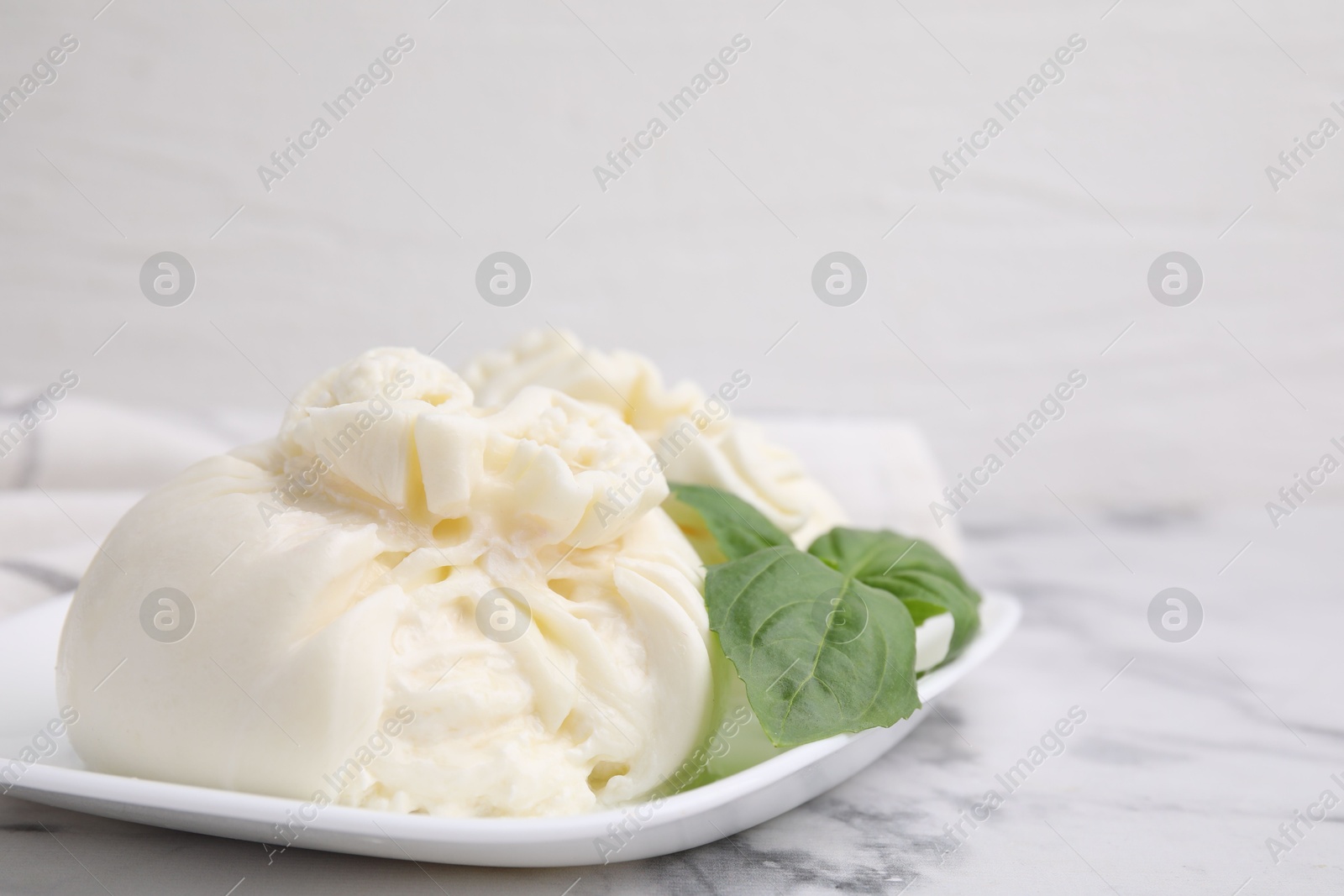 Photo of Delicious burrata cheese and basil on white marble table, closeup. Space for text