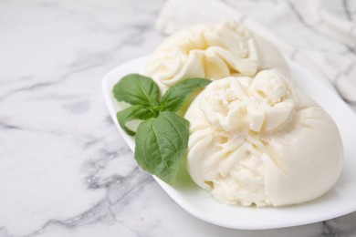 Photo of Delicious burrata cheese and basil on white marble table, closeup. Space for text