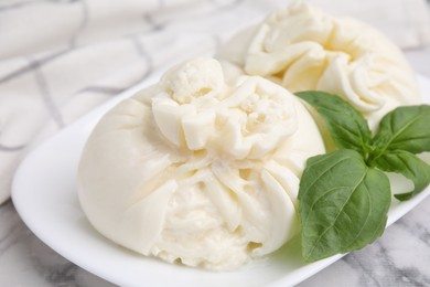Photo of Delicious burrata cheese and basil on white marble table, closeup