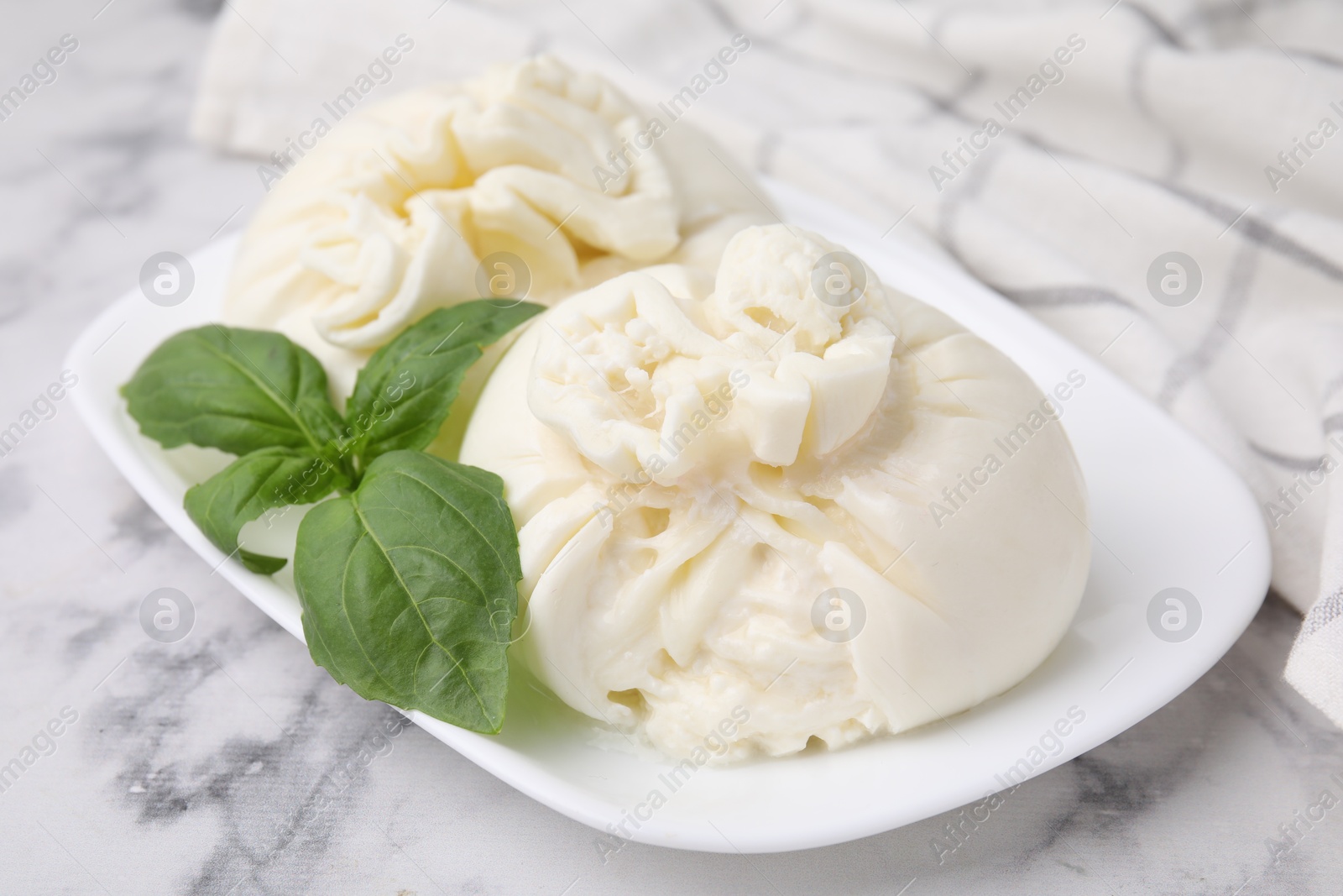 Photo of Delicious burrata cheese and basil on white marble table, closeup