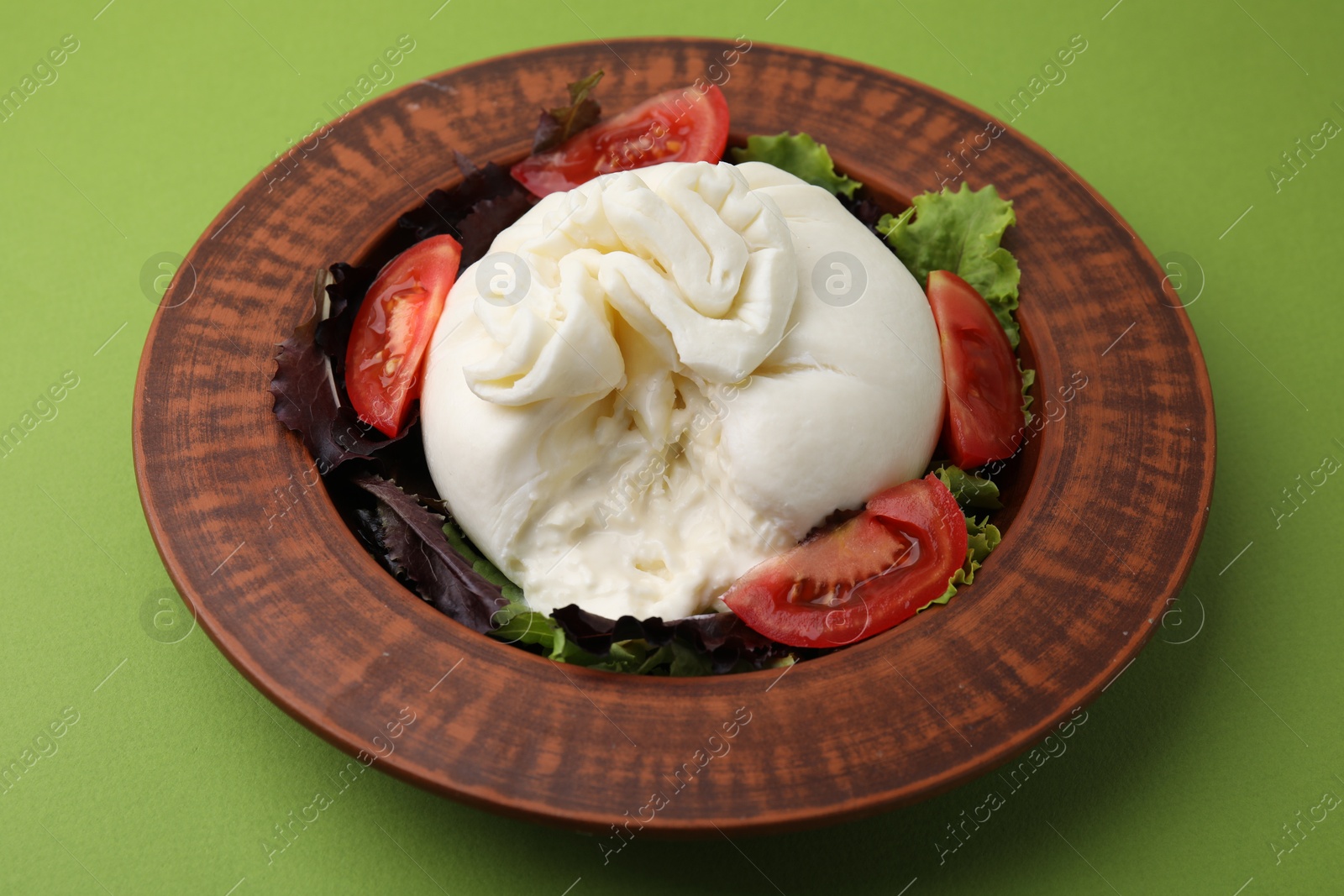 Photo of Delicious burrata salad in bowl on green table, closeup