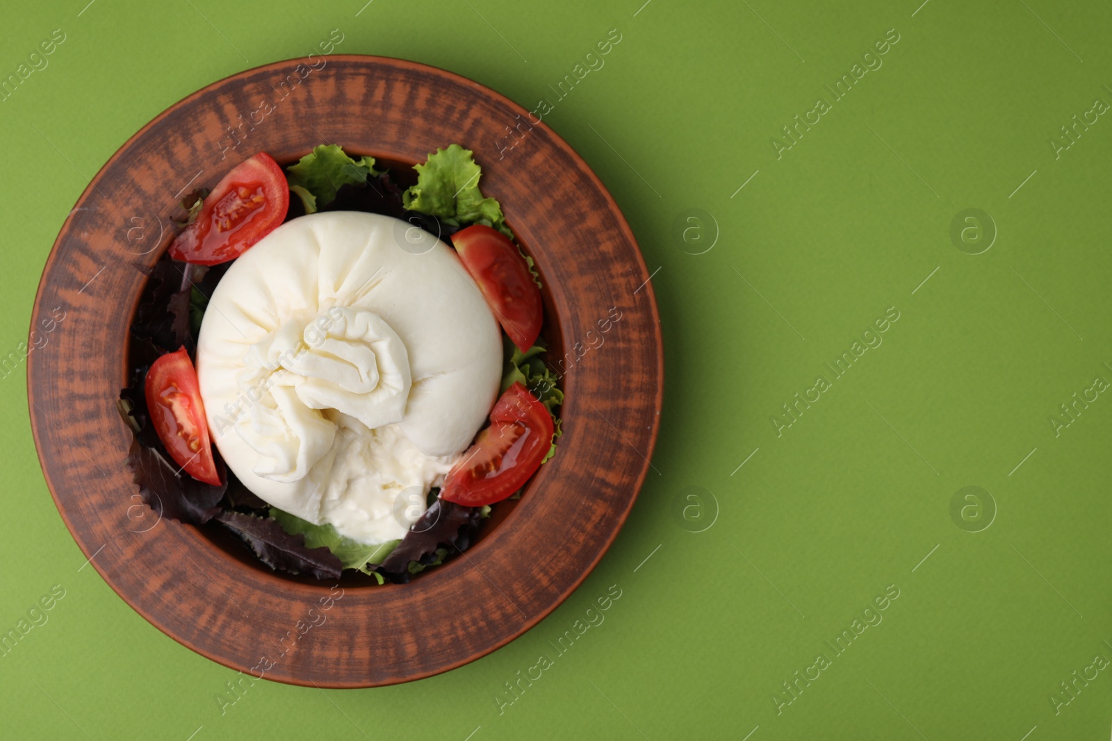 Photo of Delicious burrata salad in bowl on green table, top view. Space for text