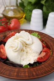 Photo of Delicious burrata salad in bowl on table, closeup