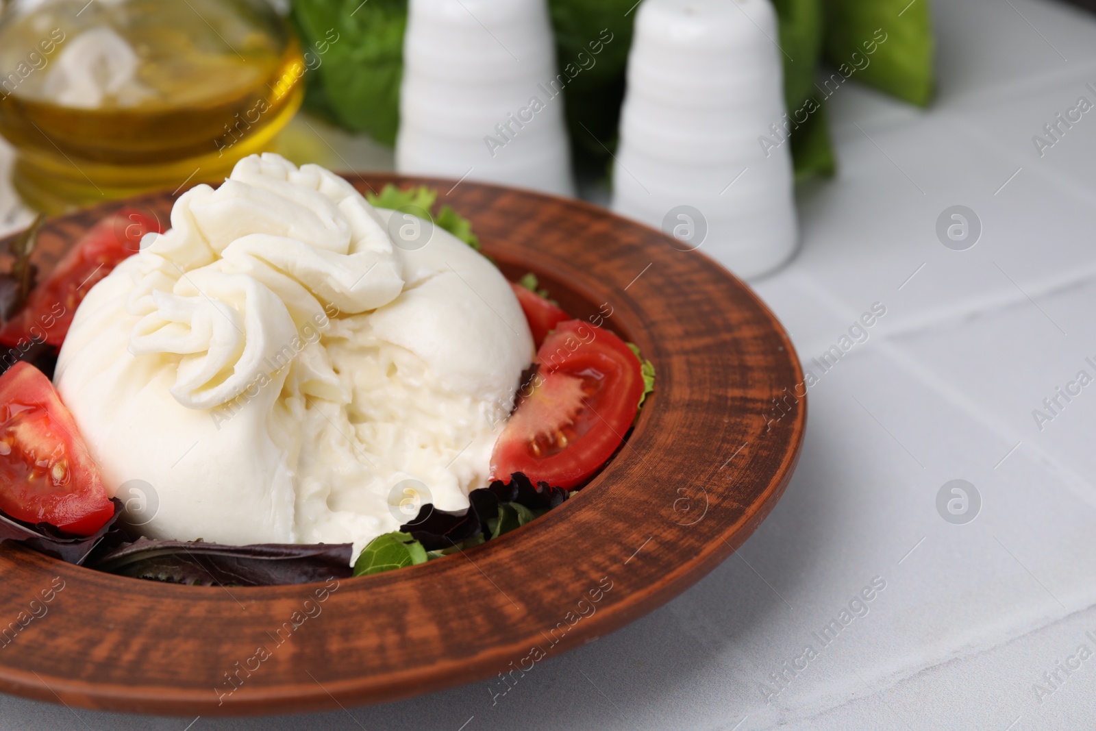 Photo of Delicious burrata salad in bowl on white tiled table, closeup. Space for text