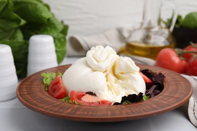 Photo of Delicious burrata salad in bowl on white table, closeup