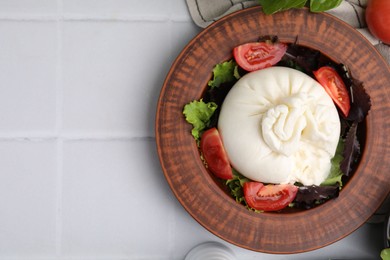 Photo of Delicious burrata salad in bowl on white tiled table, top view. Space for text