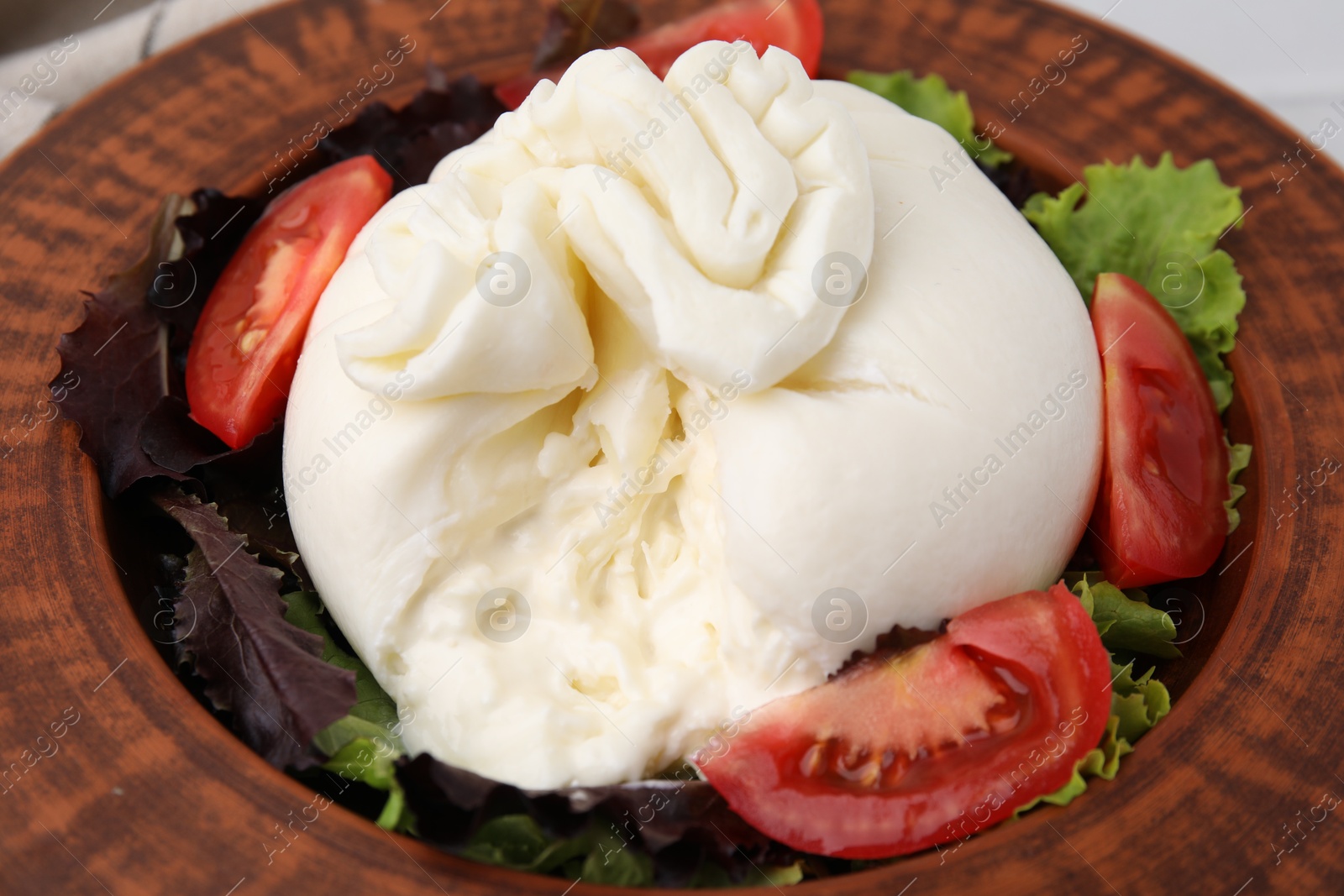 Photo of Delicious burrata salad in bowl on table, closeup