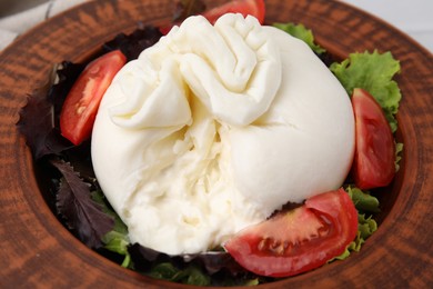 Photo of Delicious burrata salad in bowl on table, closeup