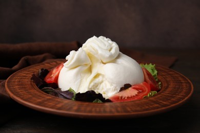 Photo of Delicious burrata salad in bowl on wooden table, closeup