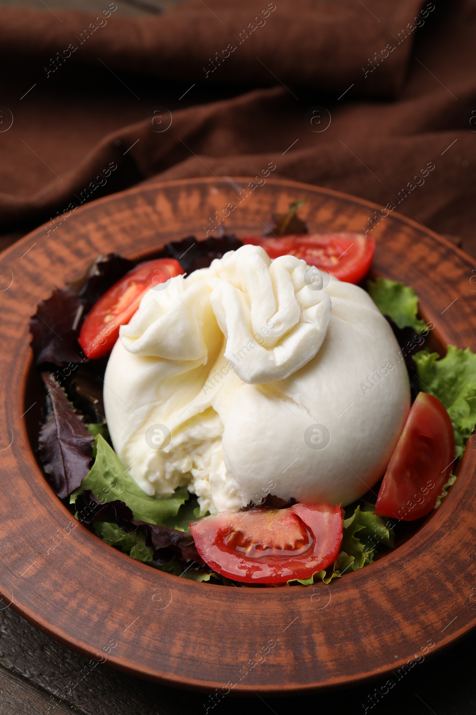 Photo of Fresh delicious burrata salad in bowl on table, closeup