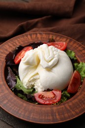 Photo of Fresh delicious burrata salad in bowl on table, closeup