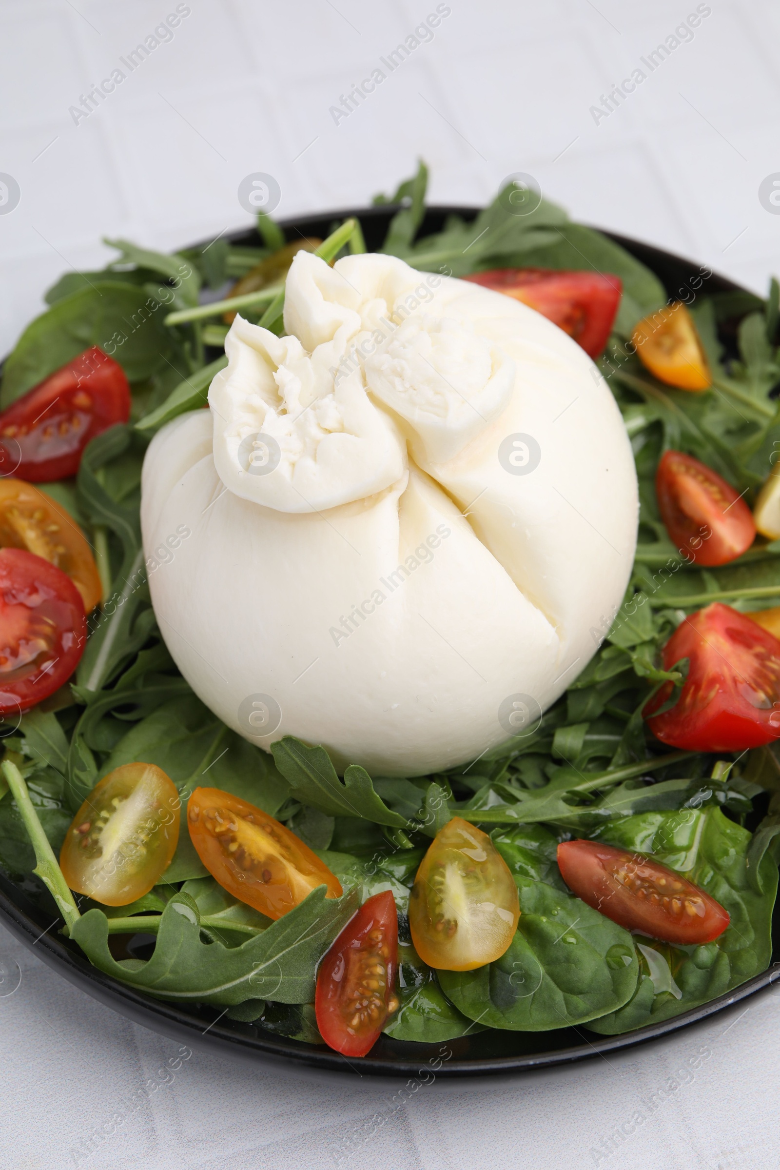 Photo of Delicious burrata salad on white tiled table, closeup