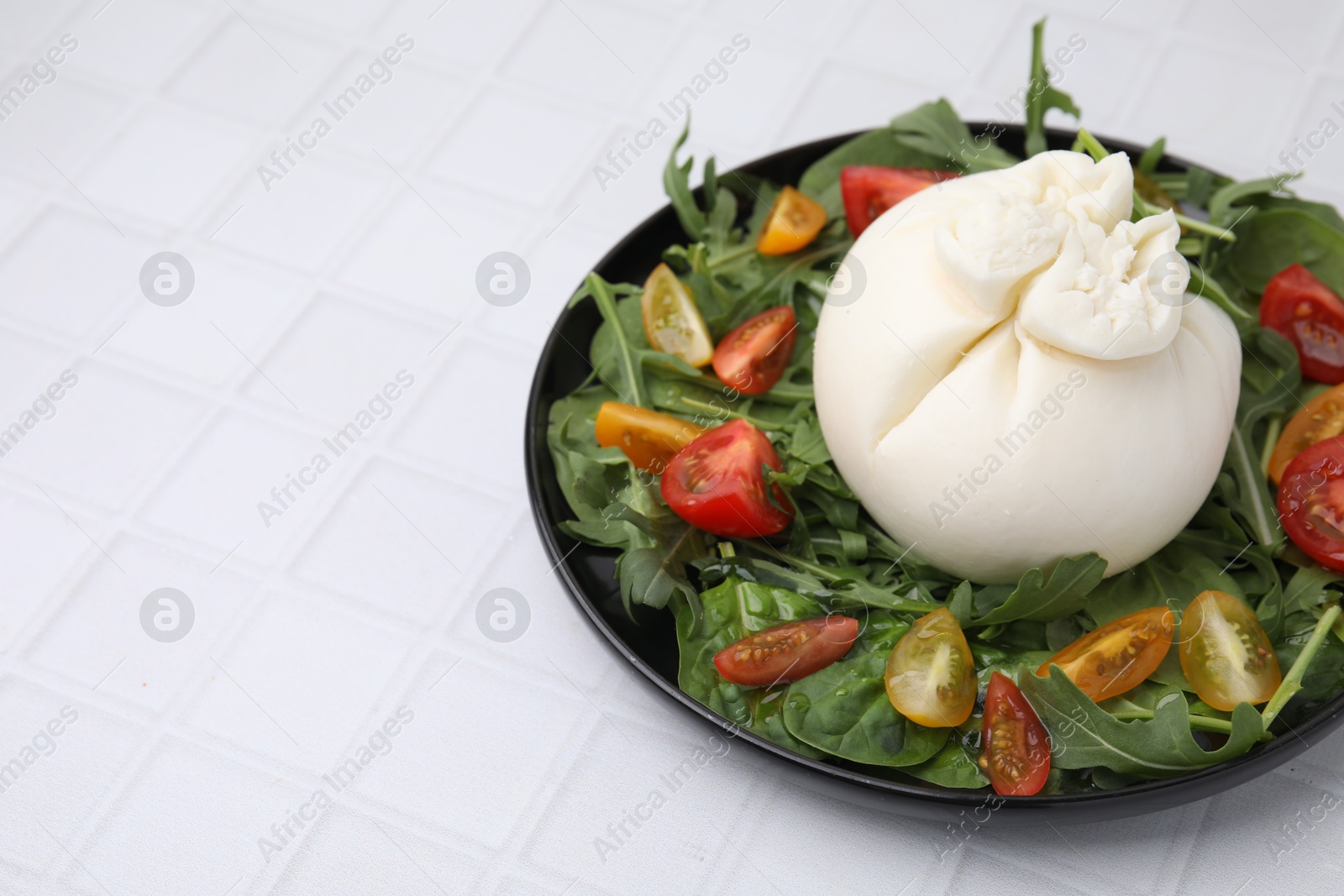 Photo of Delicious burrata salad on white tiled table, closeup. Space for text