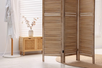 Wooden folding screen and vase with cotton branches on cabinet indoors