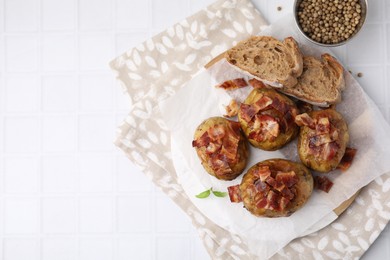 Delicious baked potatoes with bacon, bread and peppercorns on white tiled table, flat lay. Space for text