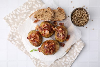 Delicious baked potatoes with bacon, bread and peppercorns on white tiled table, flat lay