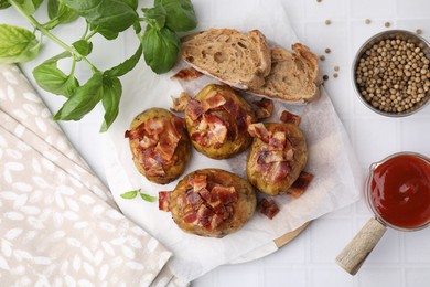 Delicious baked potatoes with bacon, bread and ketchup on white tiled table, flat lay