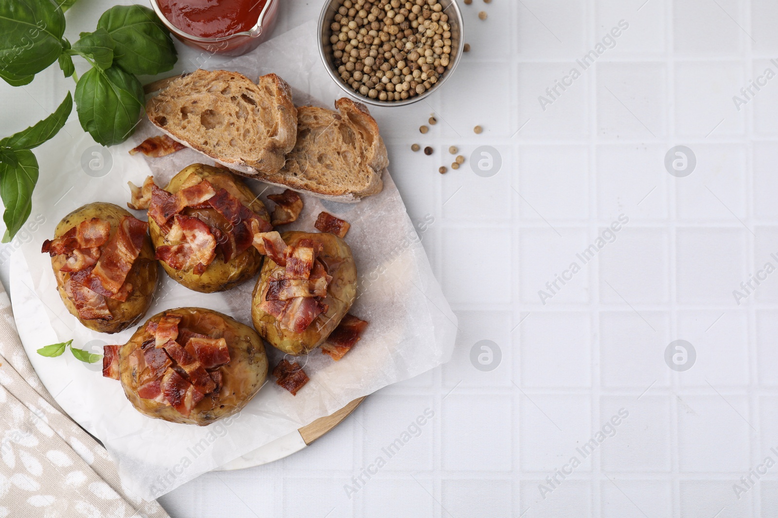 Photo of Delicious baked potatoes with bacon, bread and peppercorns on white tiled table, flat lay. Space for text