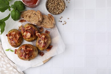 Delicious baked potatoes with bacon, bread and peppercorns on white tiled table, flat lay. Space for text