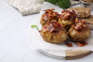 Delicious baked potatoes with bacon on white tiled table, closeup. Space for text