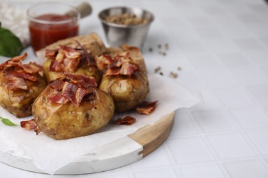 Delicious baked potatoes with bacon on white tiled table, closeup. Space for text