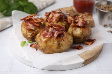 Photo of Delicious baked potatoes with bacon on white tiled table, closeup