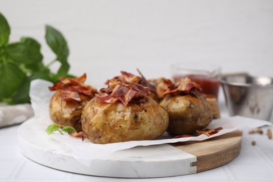 Delicious baked potatoes with bacon on white tiled table, closeup