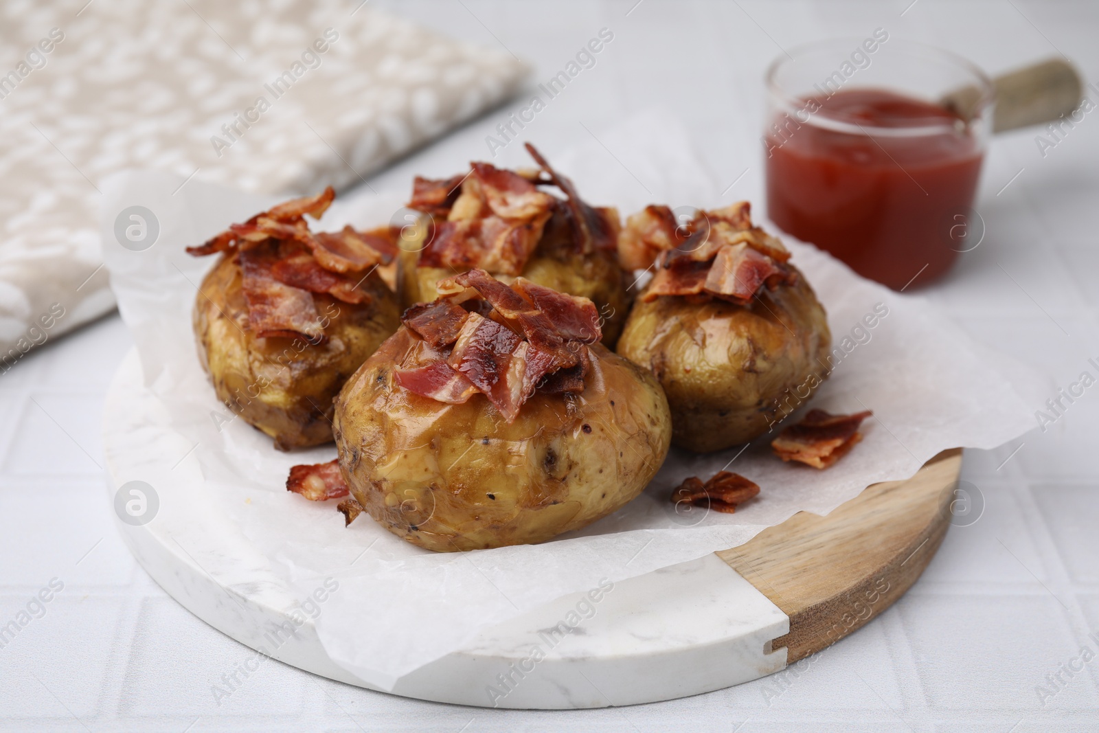 Photo of Delicious baked potatoes with bacon on white tiled table, closeup