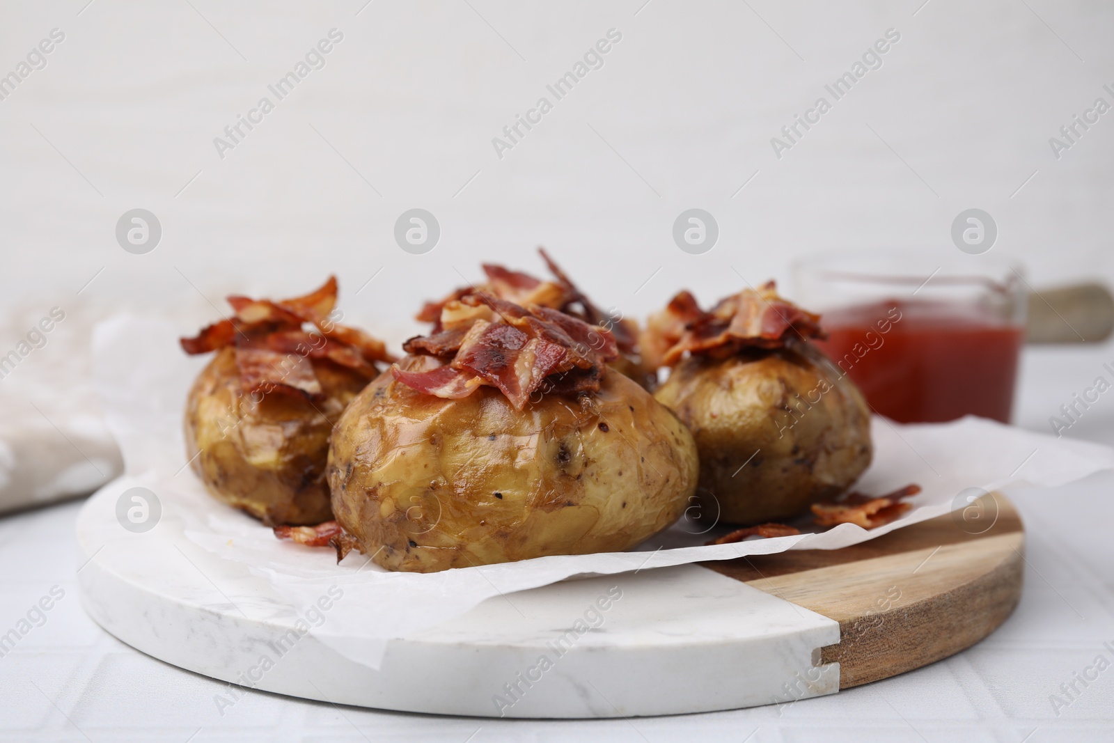 Photo of Delicious baked potatoes with bacon on white tiled table, closeup