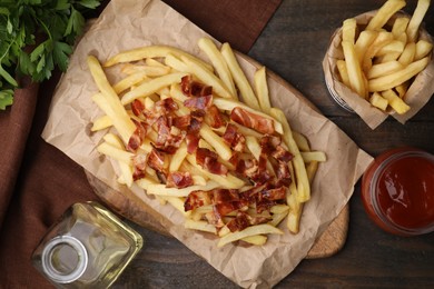 Photo of Delicious French fries with slices of bacon and ketchup on wooden table, flat lay