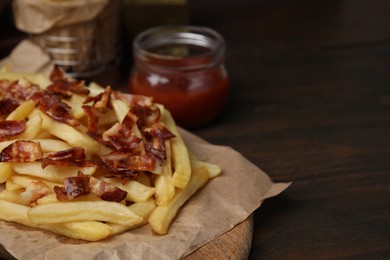 Delicious French fries with slices of bacon on wooden table, closeup. Space for text