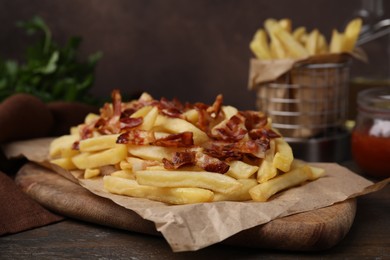 Delicious French fries with slices of bacon on wooden table, closeup