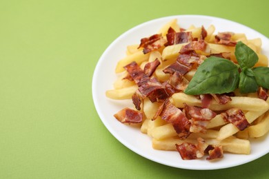 Photo of Delicious French fries with bacon and basil on green background, closeup. Space for text